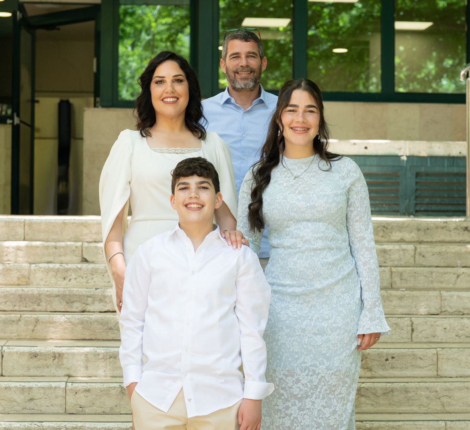 Family group sitting together on stone steps wearing coordinated light blue and white outfits.