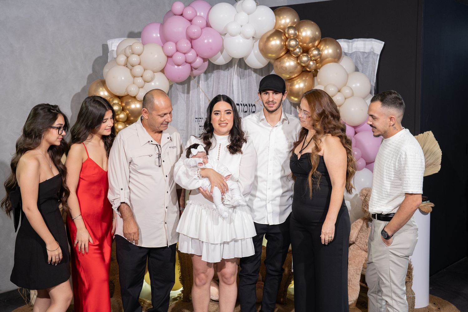 Group gathering at baby celebration event with pink and gold balloon decorations.