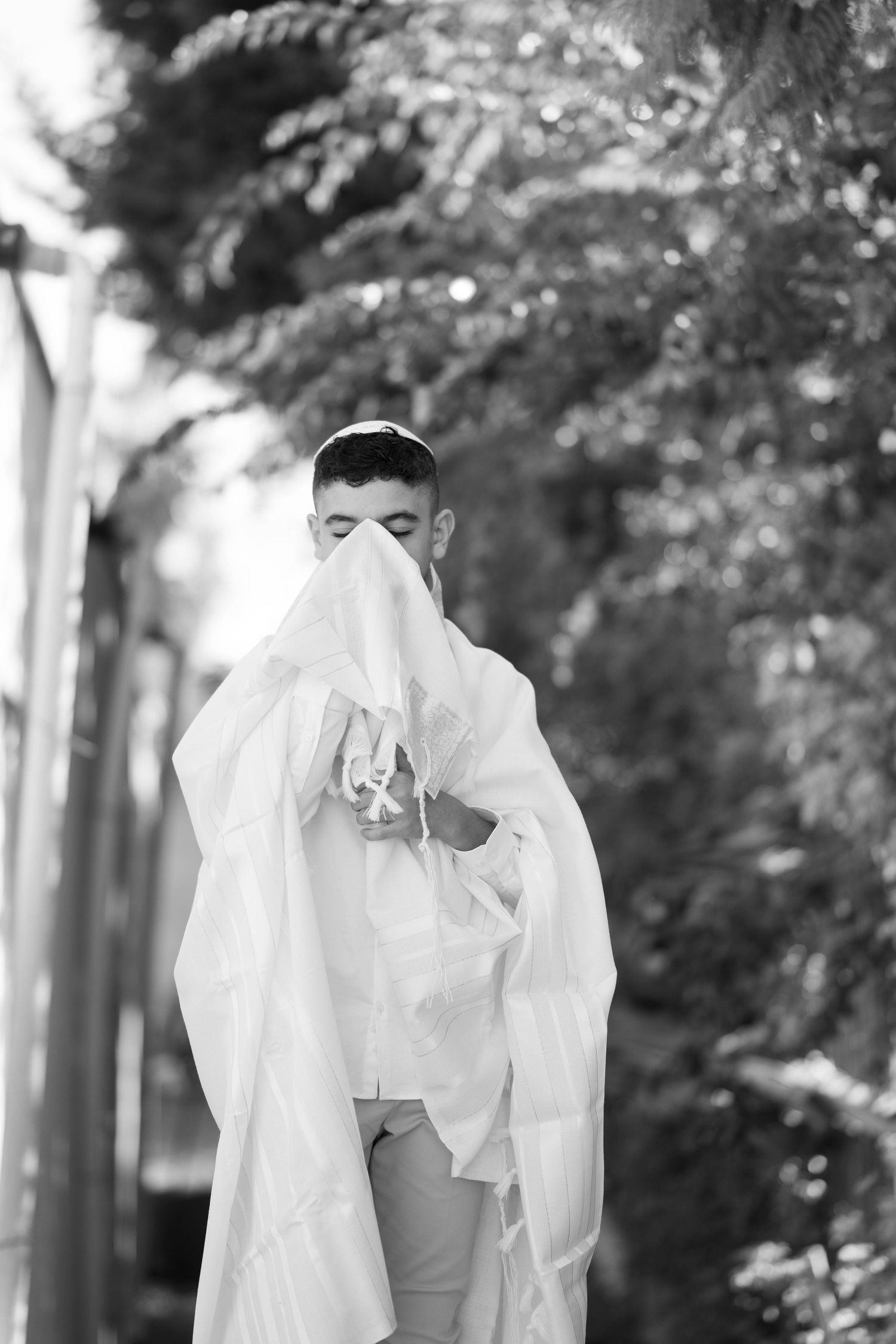 A black and white portrait of someone playfully hiding behind white fabric outdoors.