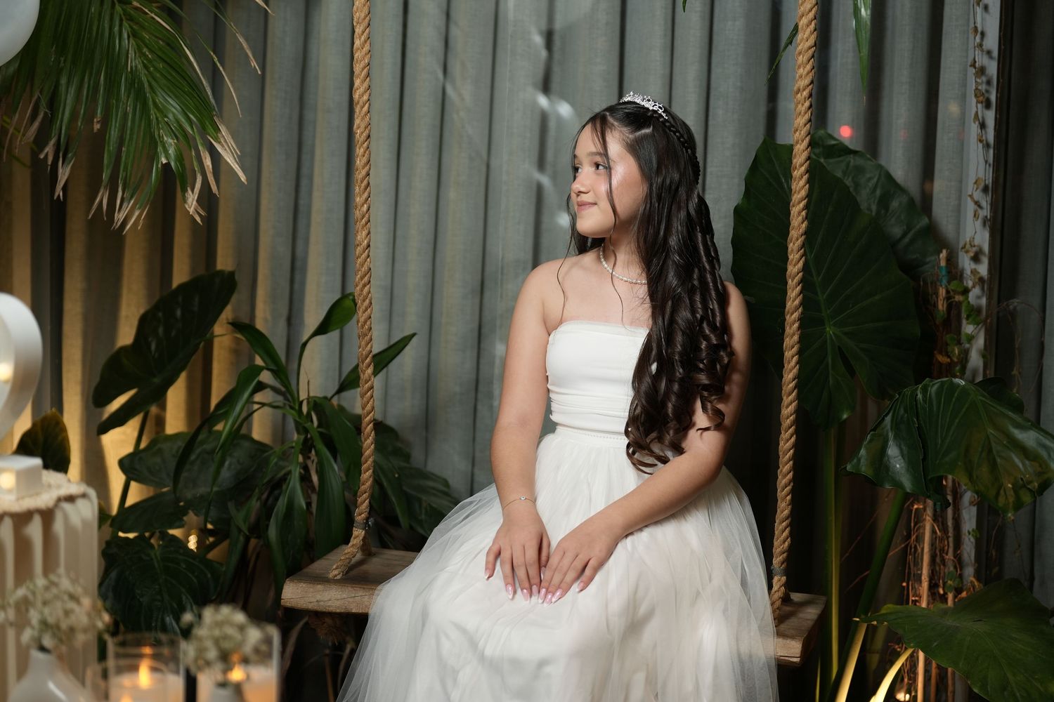 Elegant bride in a white wedding dress poses in a lush tropical garden setting with palm fronds and natural lighting.