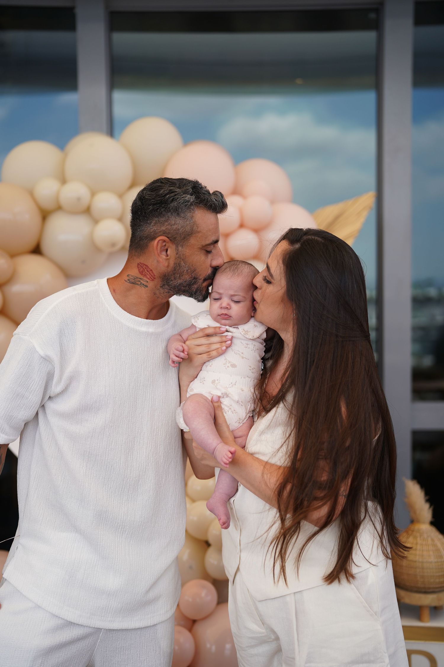 A tender family moment against a backdrop of blush and white balloons and golden palm leaves.