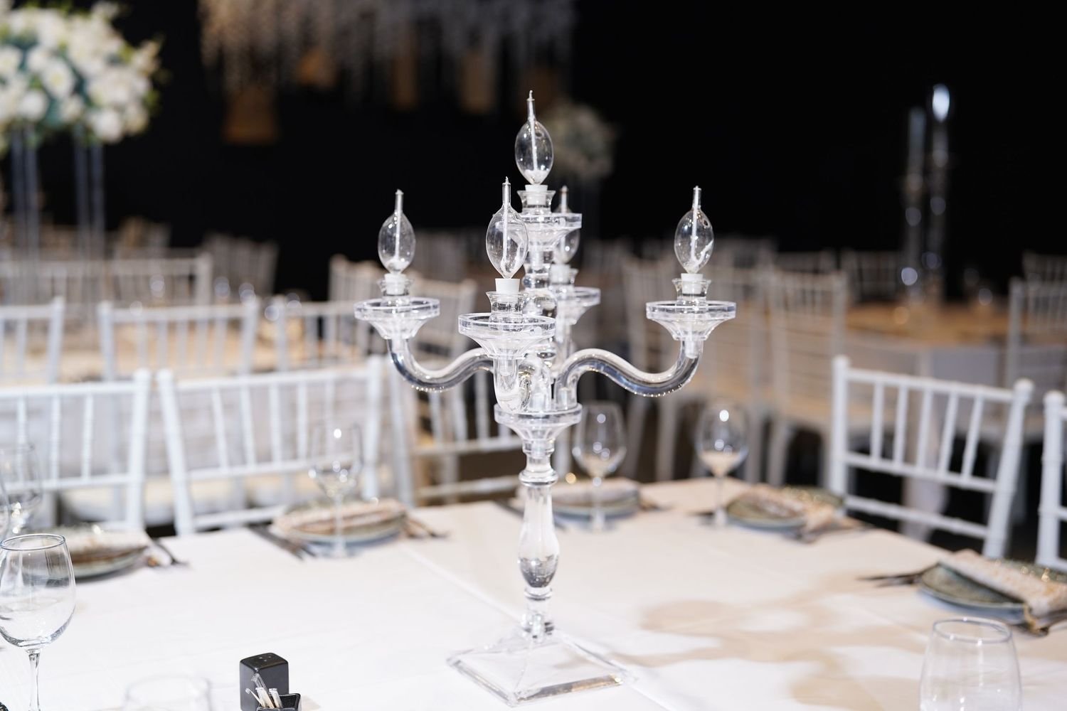 Long tables set with crystal glassware and white floral arrangements for an elegant event.