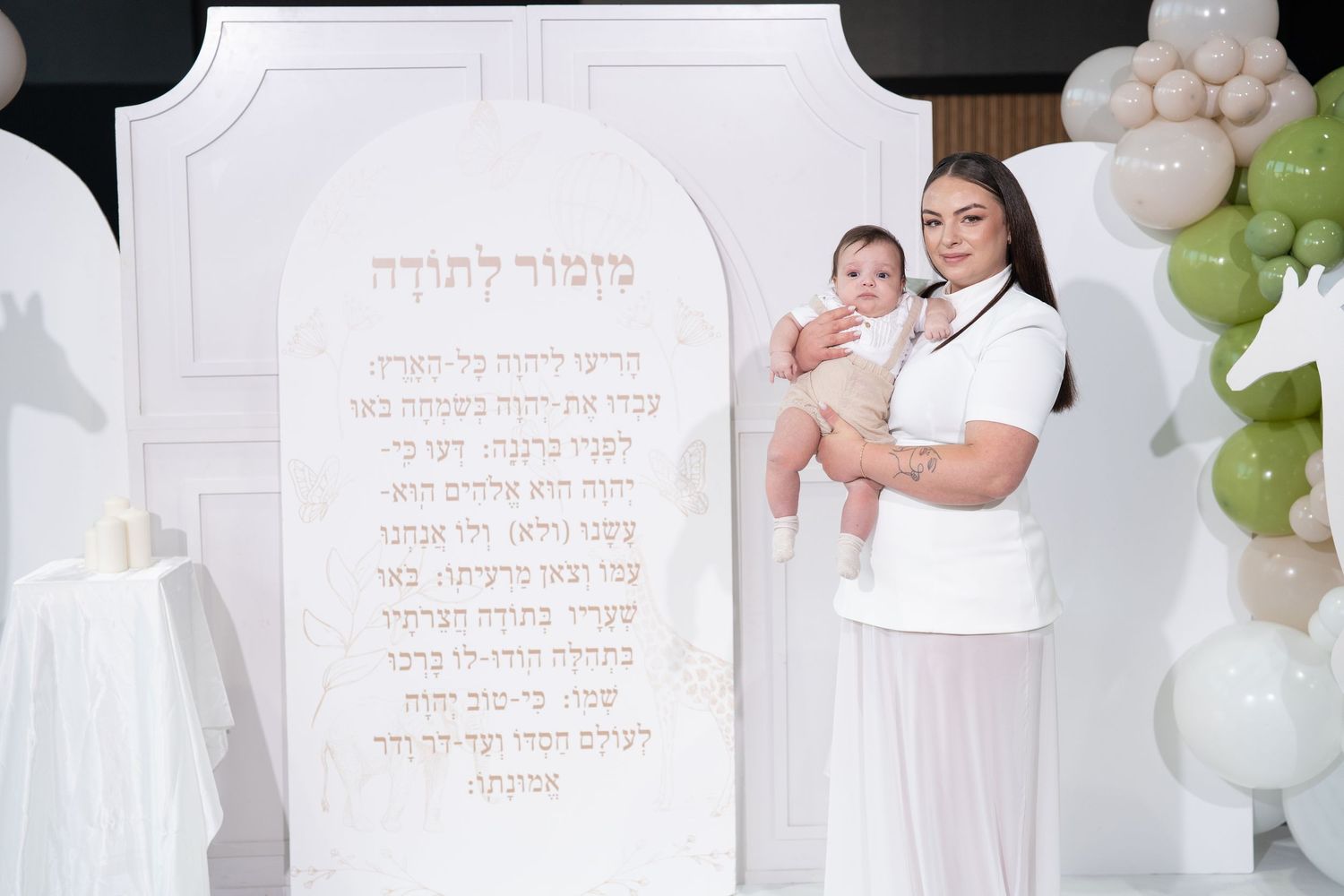 Studio photoshoot featuring Hebrew text decorations and elegant white balloon arrangements.