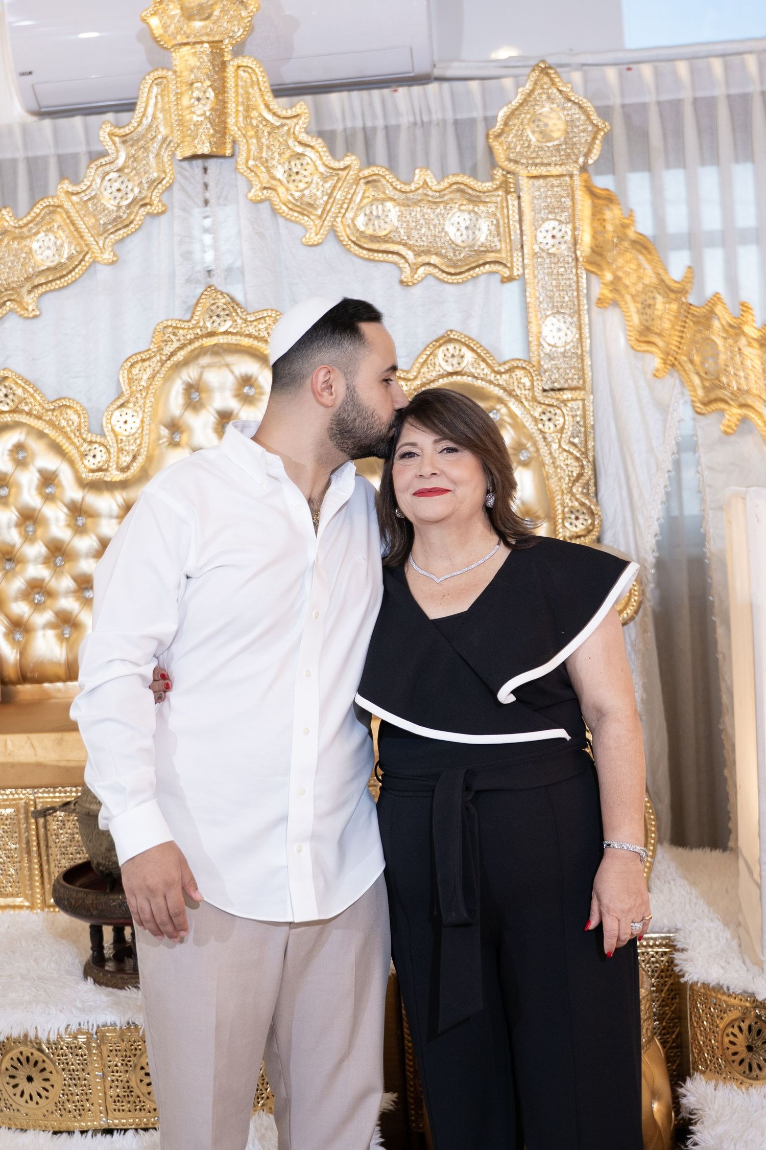 Couple poses together in formal attire against decorative gold throne backdrop.