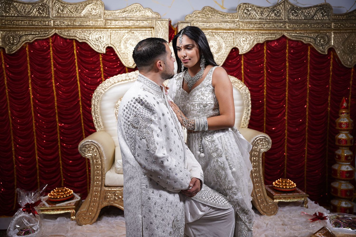 A couple shares an intimate moment while wearing coordinated white formal attire.