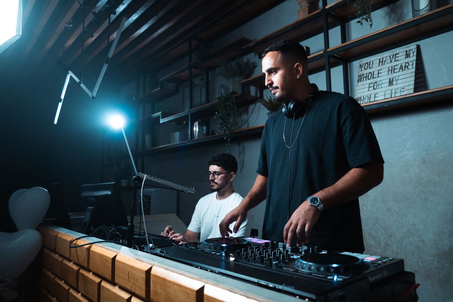 DJs performing at a dimly lit venue with professional equipment and blue lighting effects.