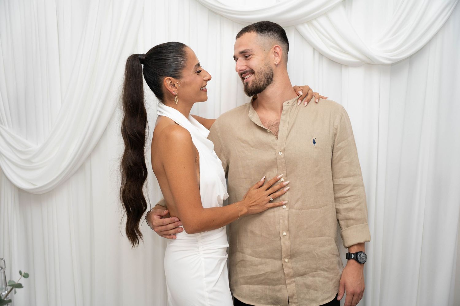 Couple sharing intimate moment against white draped backdrop at formal event.