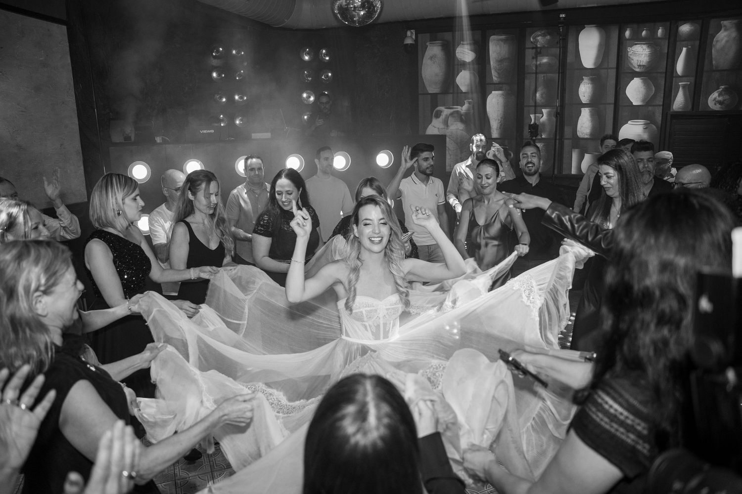 Black and white photo of wedding guests dancing under string lights at a reception.