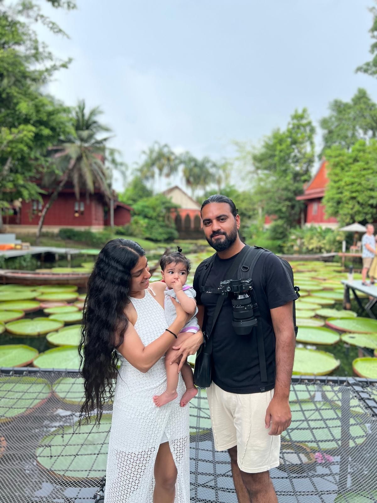 Family posing together on a deck with lush tropical garden and red buildings in background.