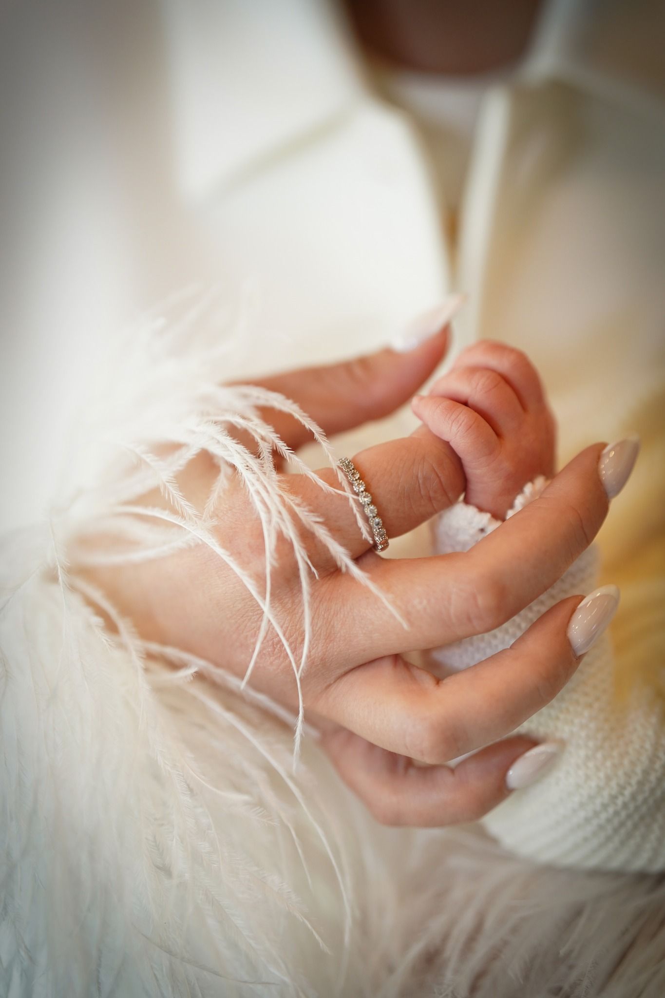 Close-up of delicate hands with ring detail against white feathery fabric.