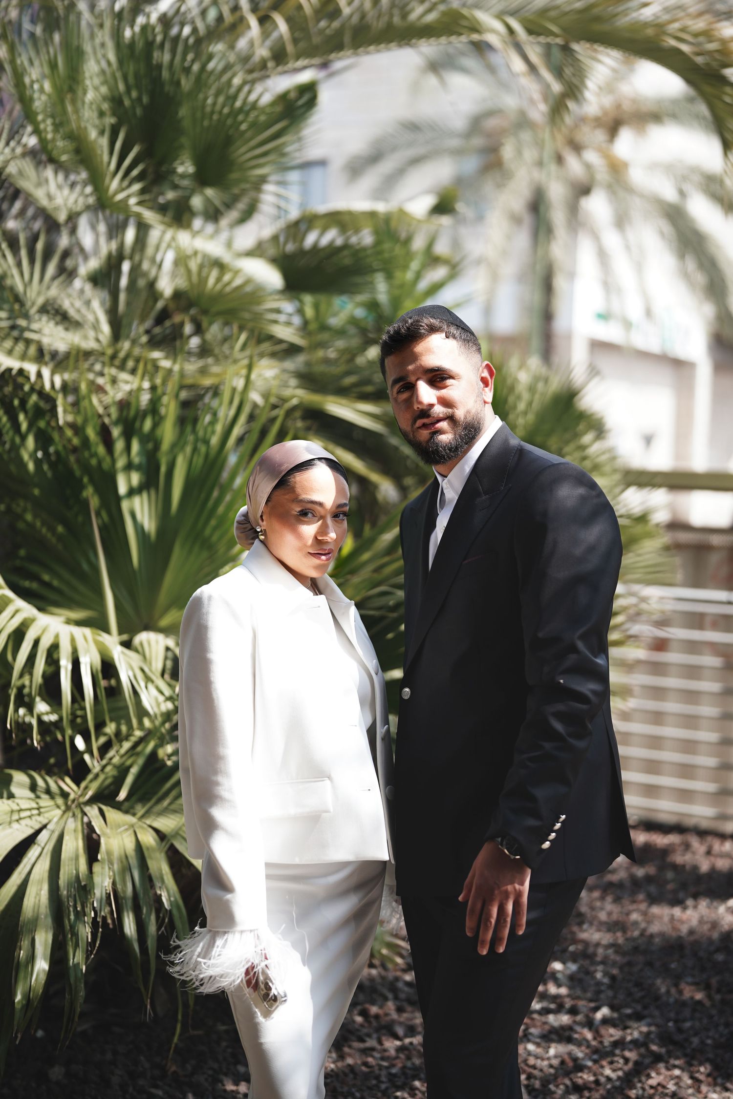 Couple poses together in formal attire against tropical garden setting.