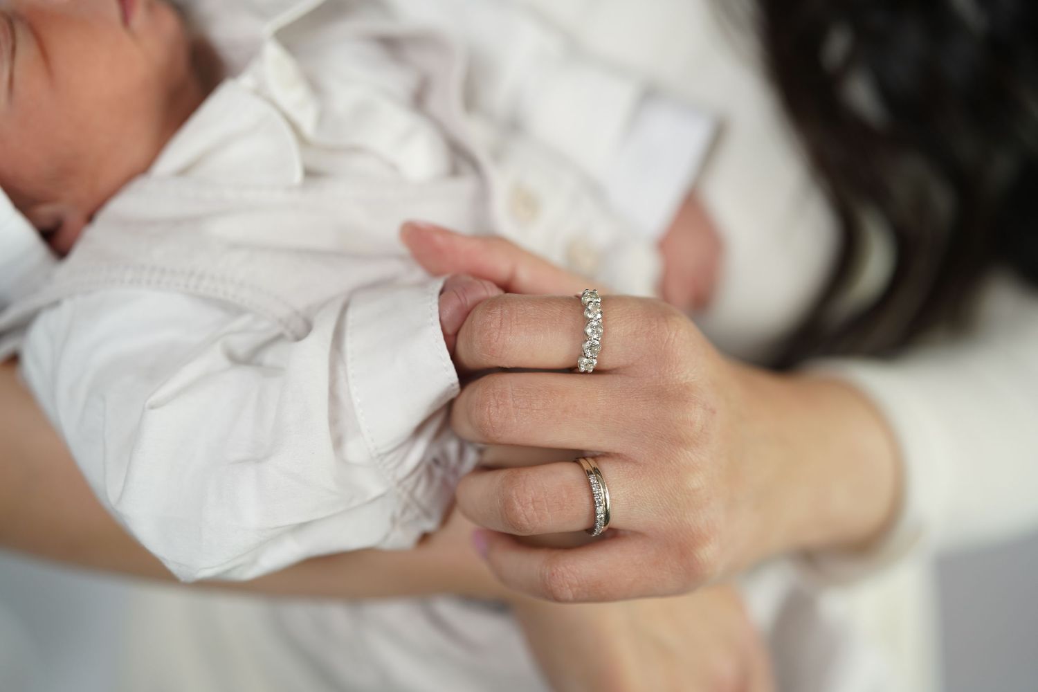 Close-up detail of hands wearing rings while holding a baby wrapped in white.