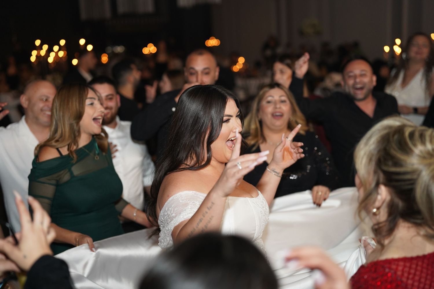 Bride in white strapless gown laughing and celebrating with guests on the dance floor at a wedding reception.