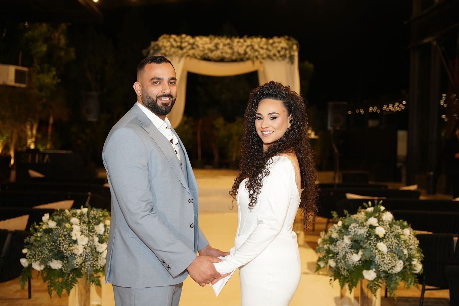 Couple in formal attire dancing together at an elegant venue with floral decorations.