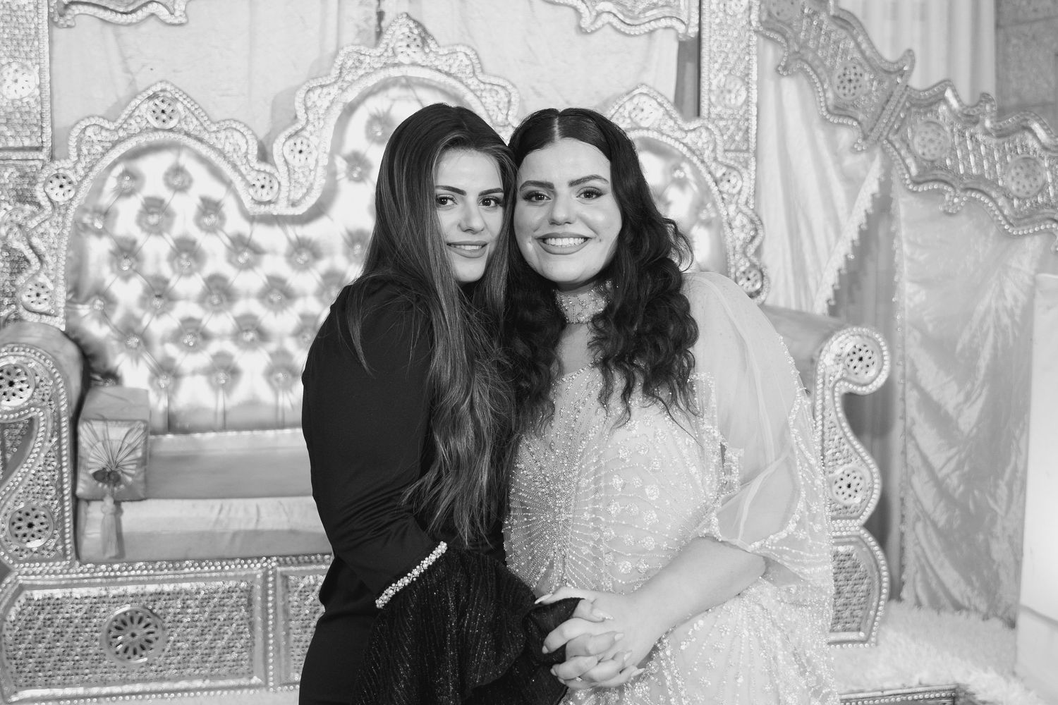 Black and white portrait of two people posing against decorative backdrop.