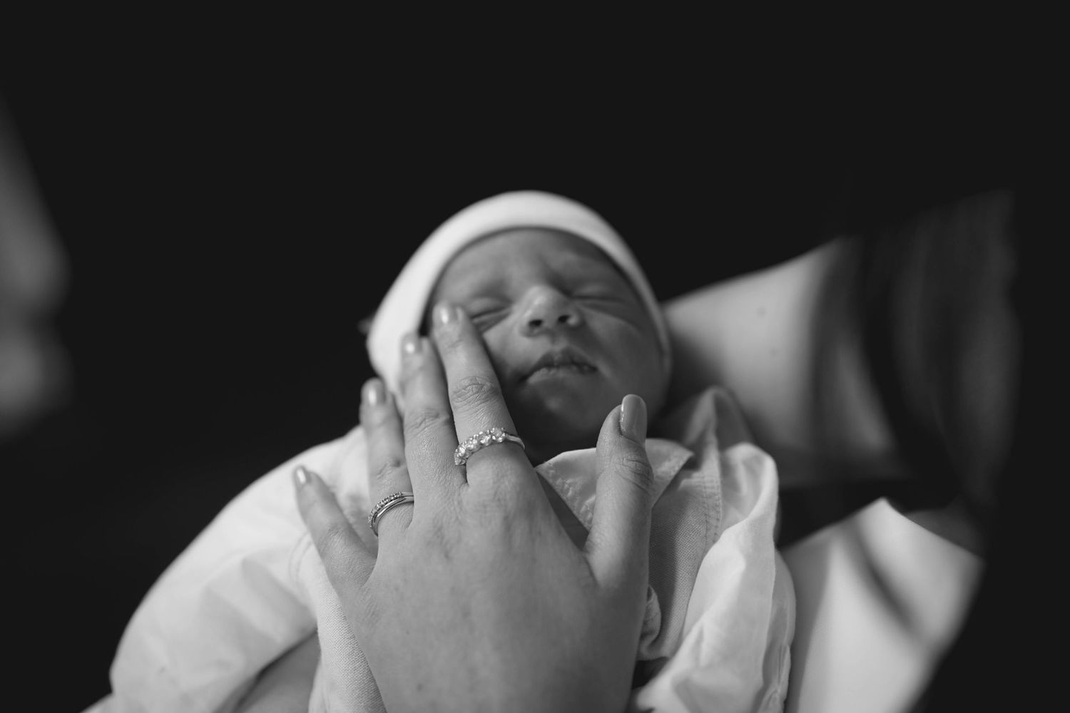 Black and white close-up photograph of a sleeping newborn in white clothing.