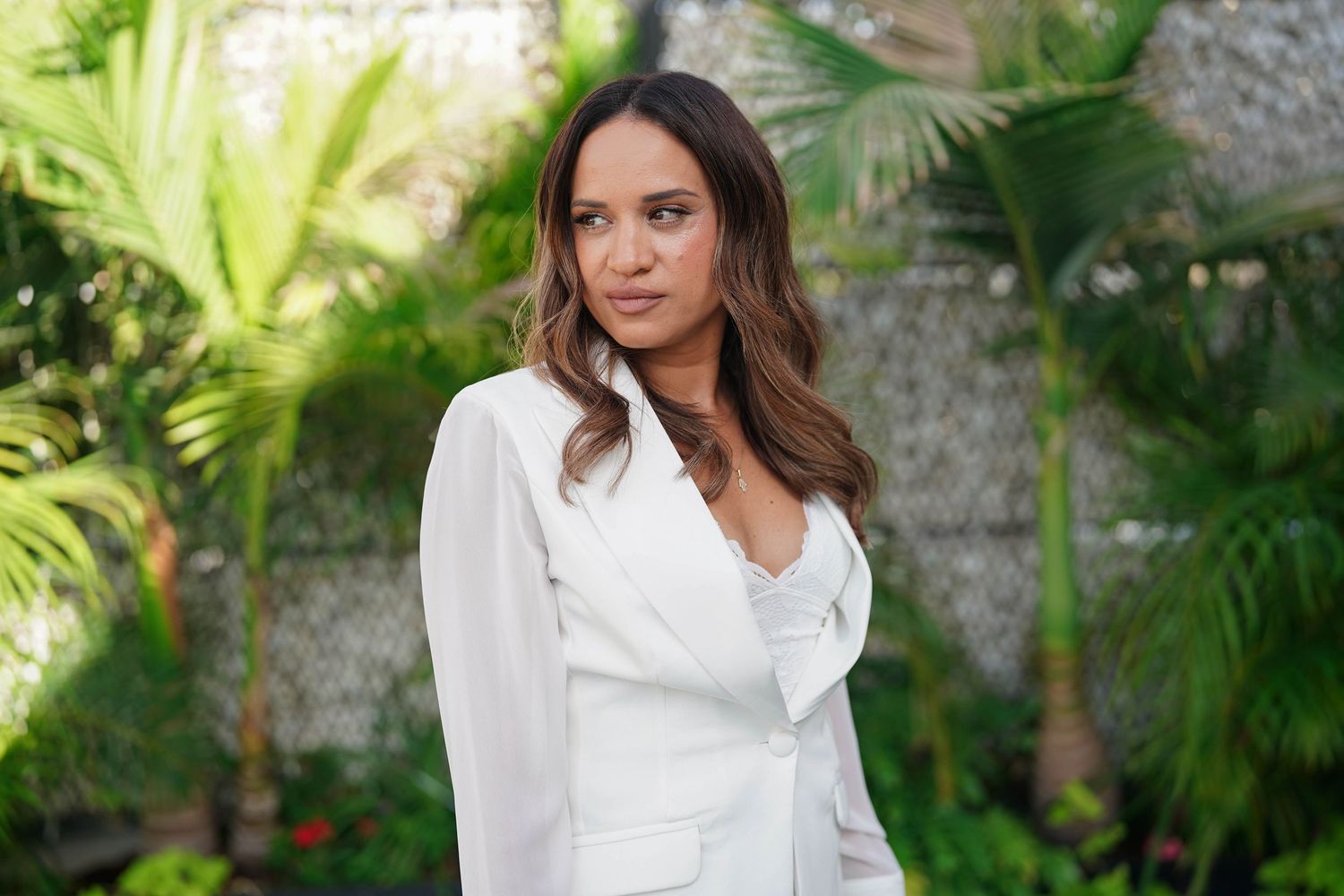 Woman in white blouse poses in front of lush tropical garden setting.