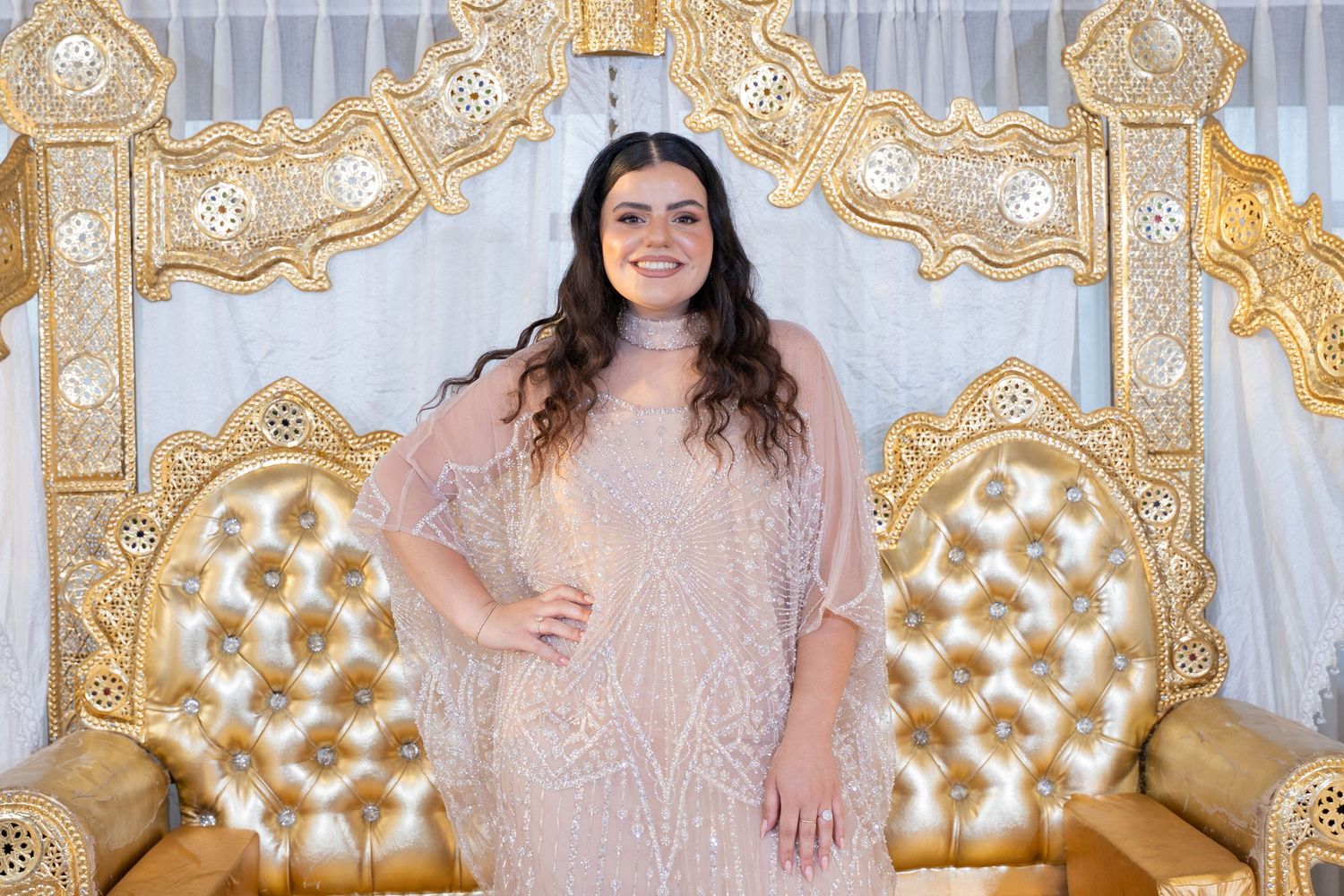 Person in sequined pink gown poses confidently against luxurious gold and white backdrop.