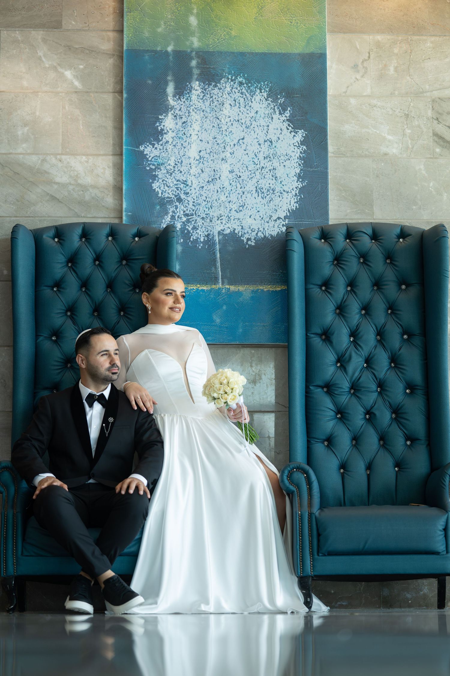 Elegant wedding portrait with tufted blue chairs and white tree artwork in the background.
