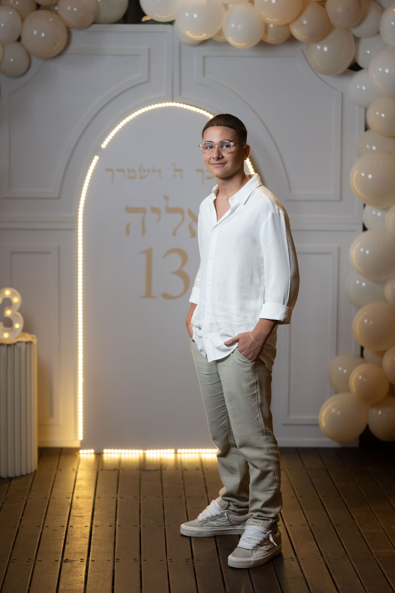 Elegant party setup with illuminated arch and white balloon decorations against paneled wall.