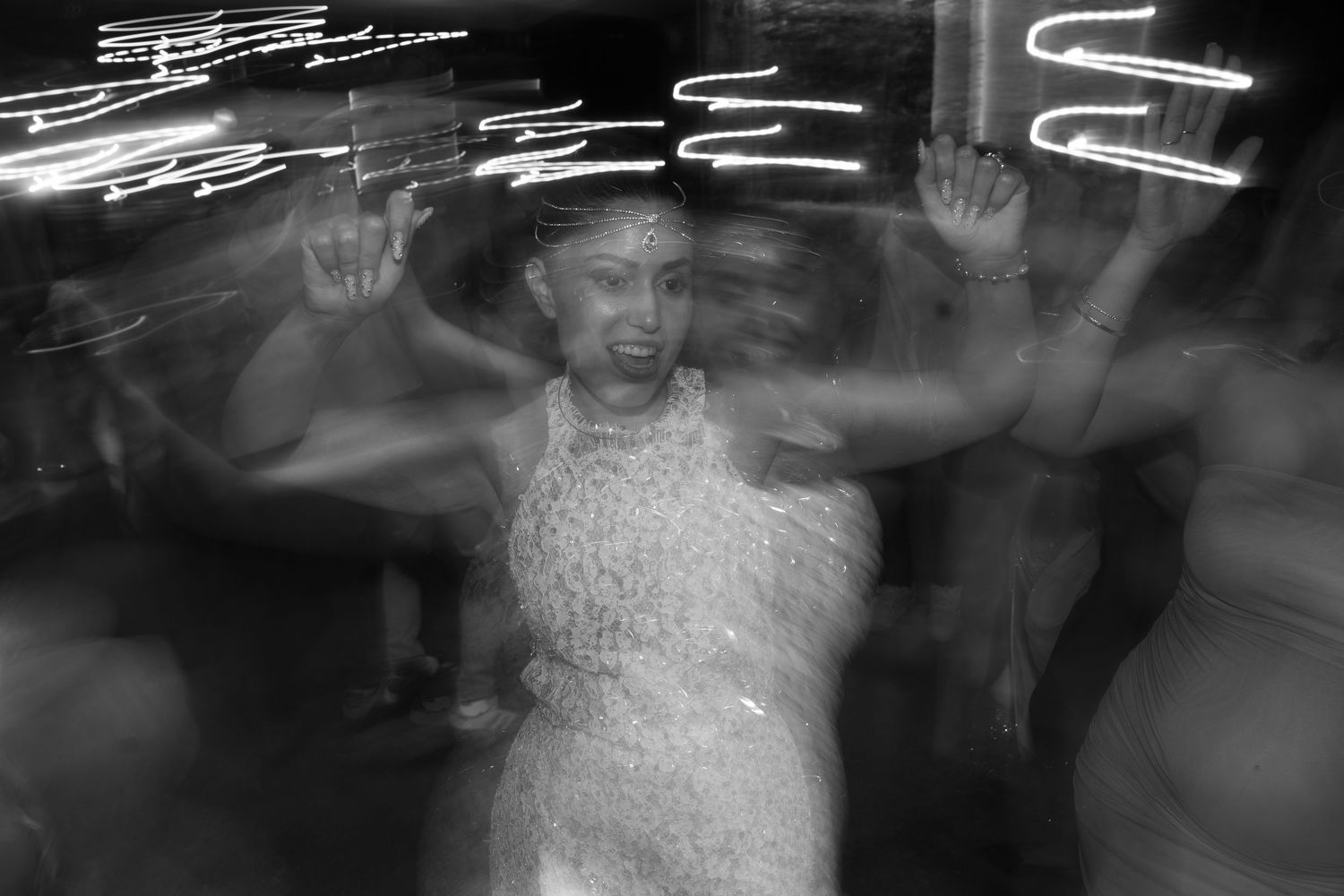 Blurred black and white photo of a woman in a lace dress dancing at a nightclub with neon lights.