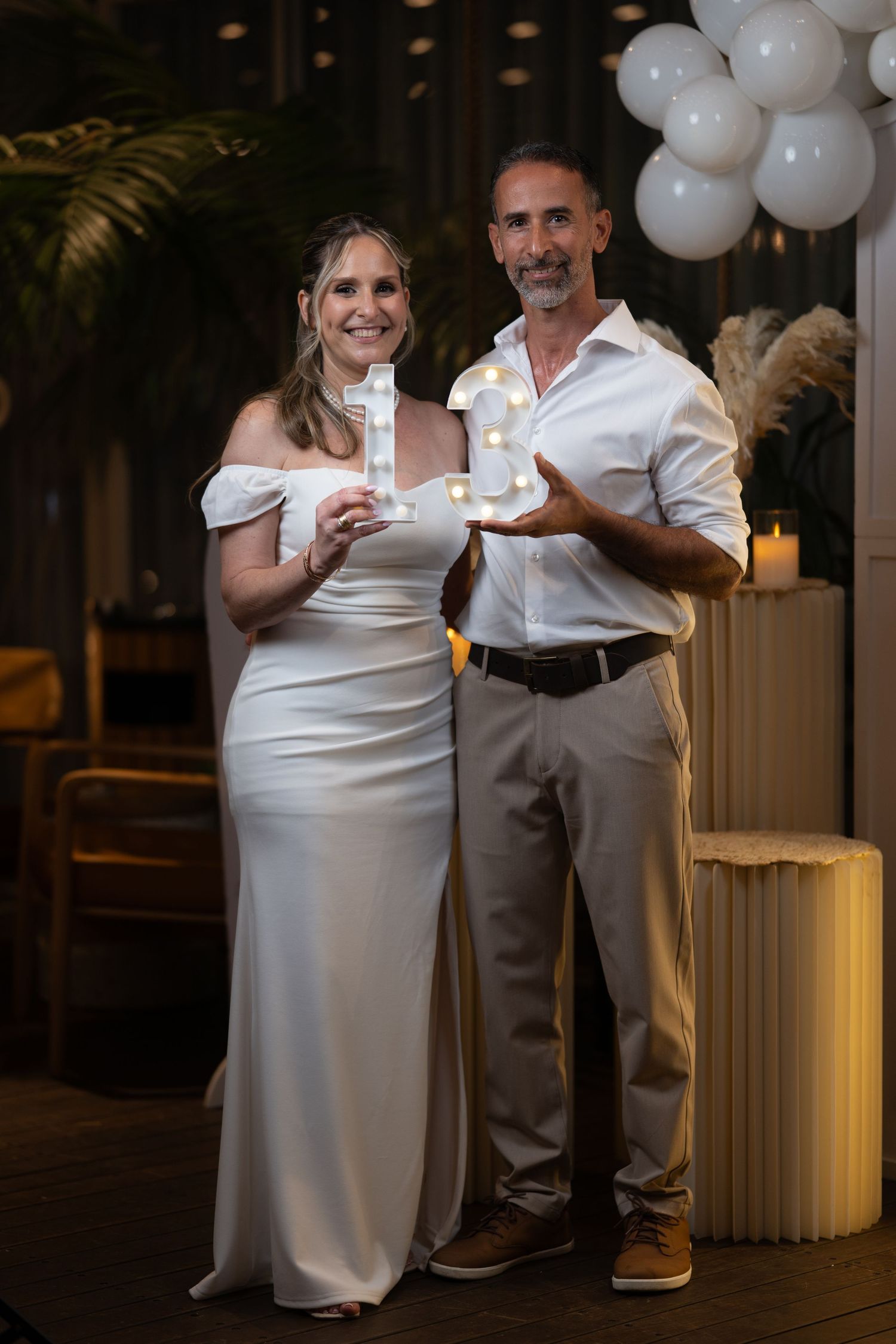 Couple sharing a sweet moment during celebration with white balloon decor and candlelight.