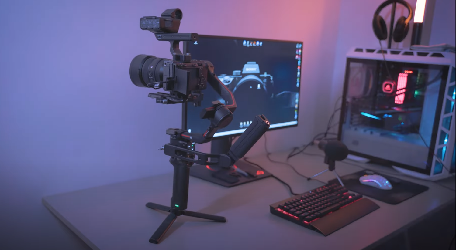 A professional camera setup with gimbal stabilizer and computer monitor in a purple-lit room.