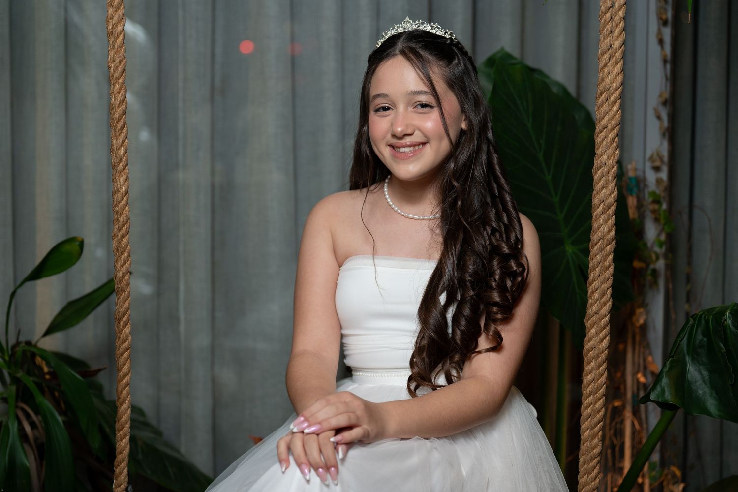 A person in a white dress stands against a curtained backdrop with hanging rope accents.