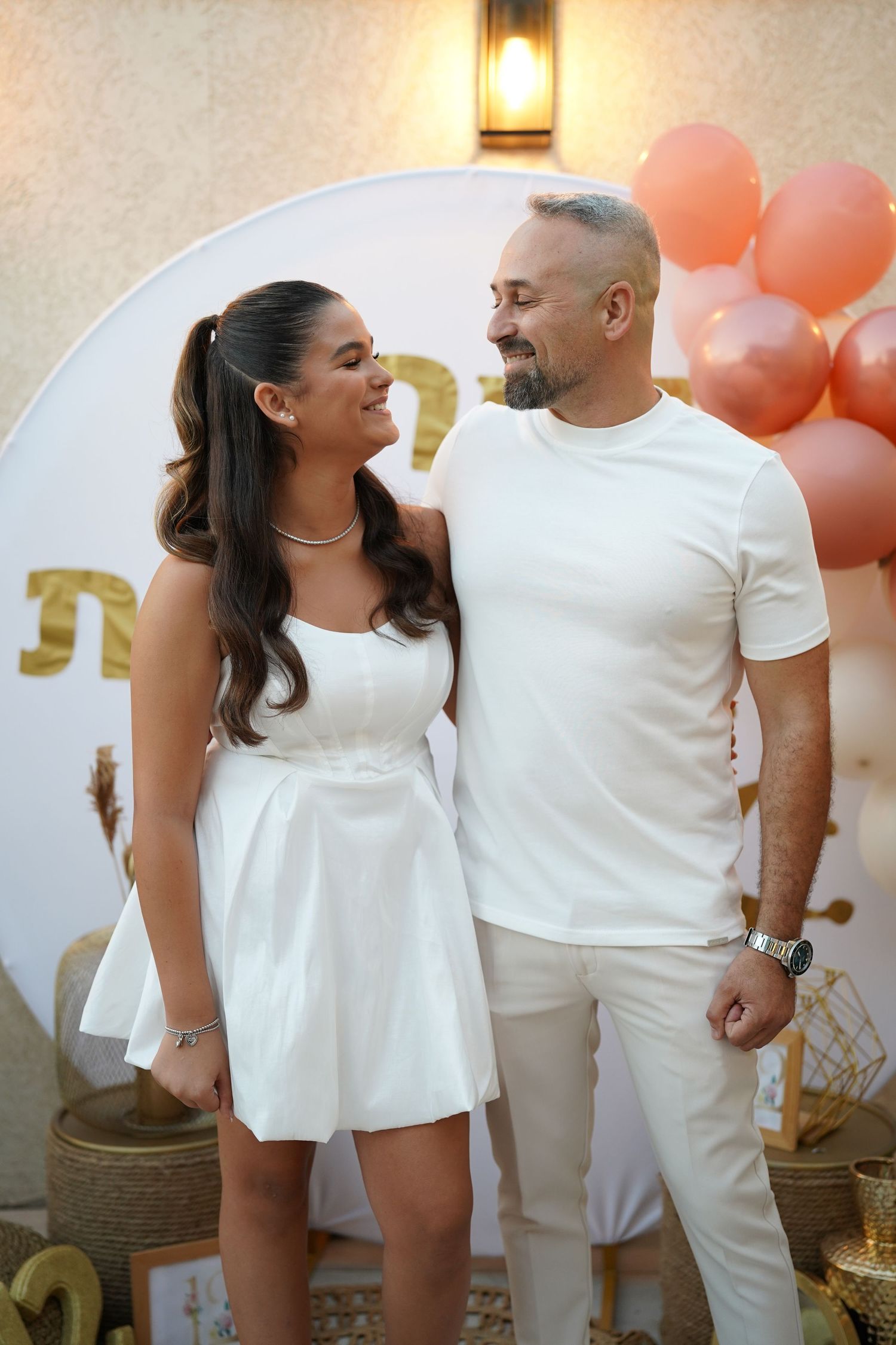 Candid moment between people in all-white outfits at a decorated outdoor venue.