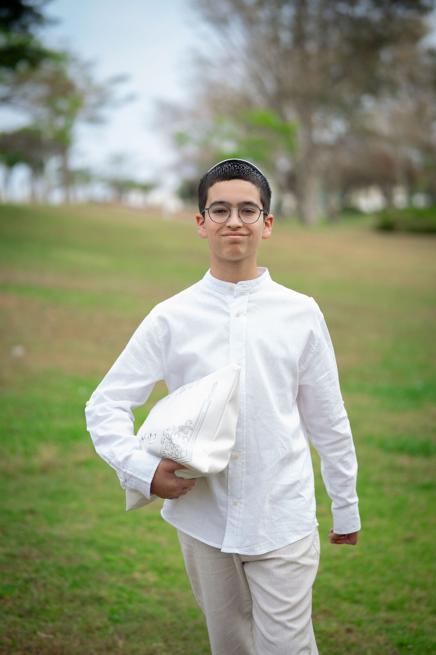 A person wearing all white clothing poses in a grassy outdoor setting.