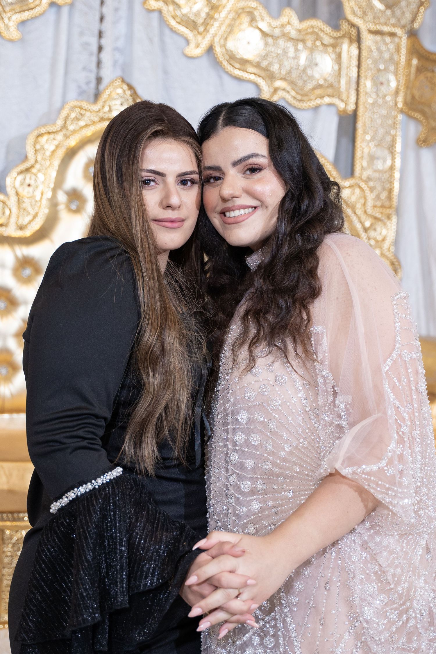 Two people posing together in formal attire against an elegant gold-patterned backdrop.
