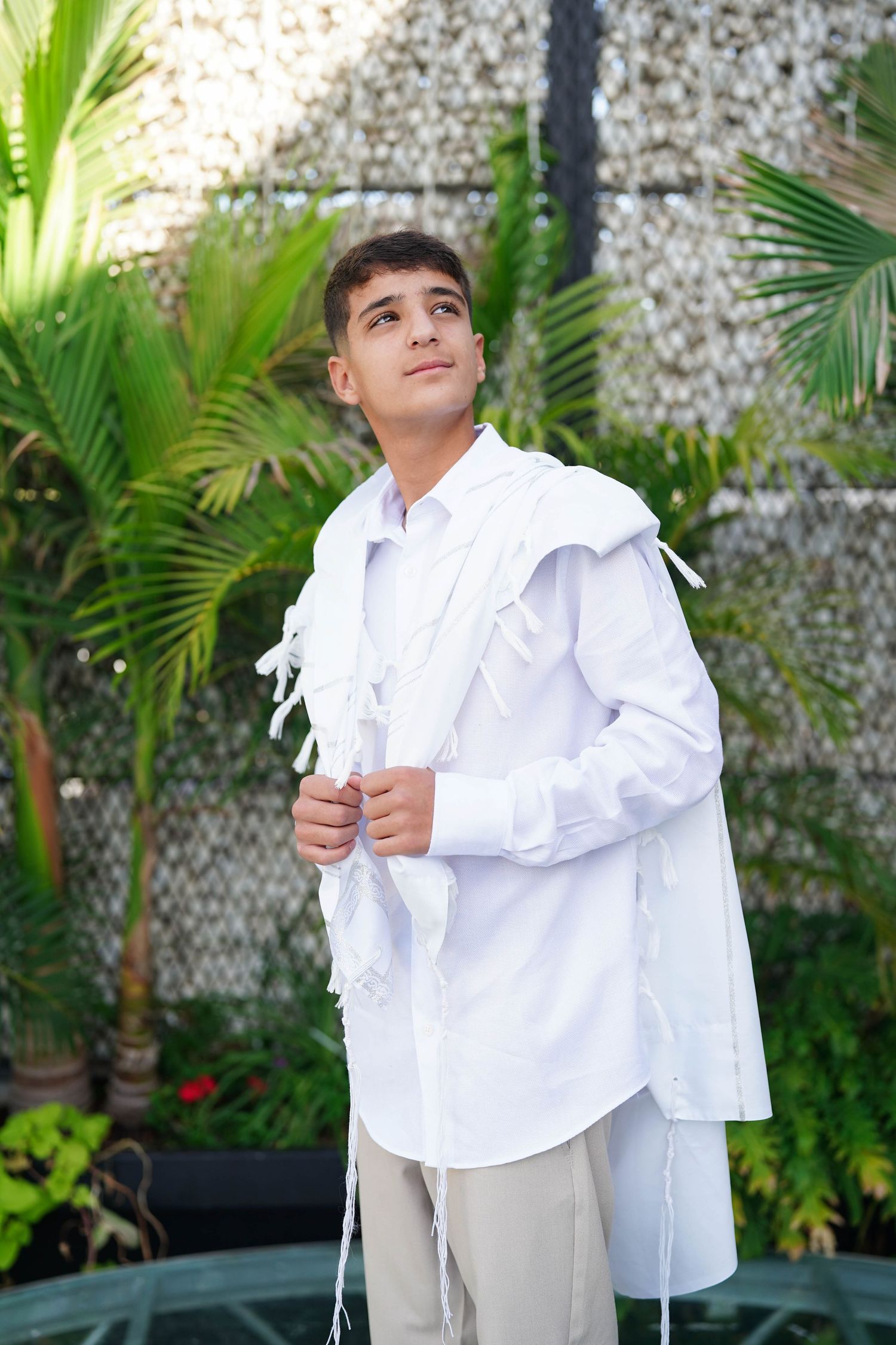 Young person in white ruffled shirt poses against tropical garden background.