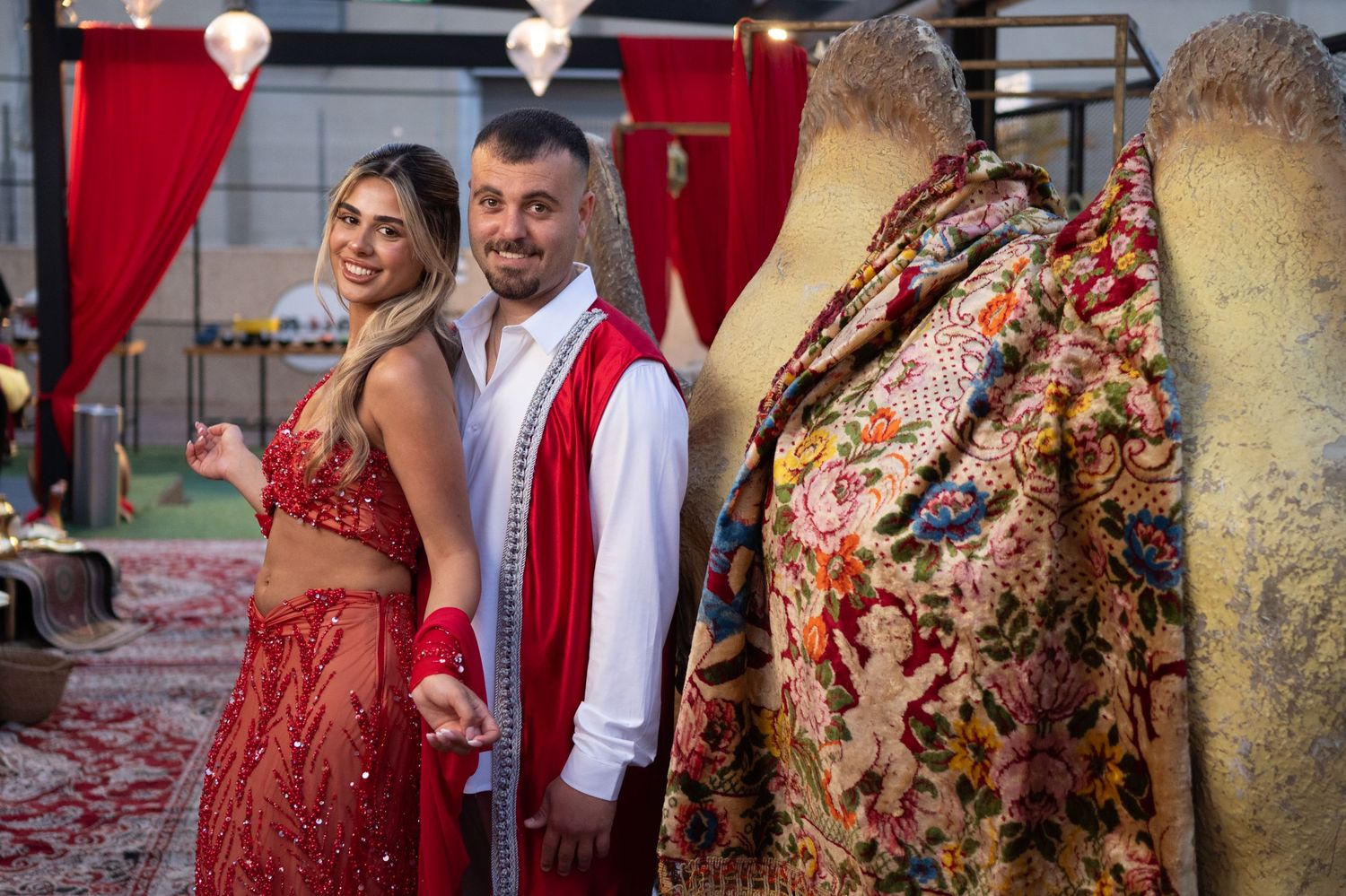 Couple in traditional Indian attire posing beside an ornate embroidered garment at a festive cultural event.