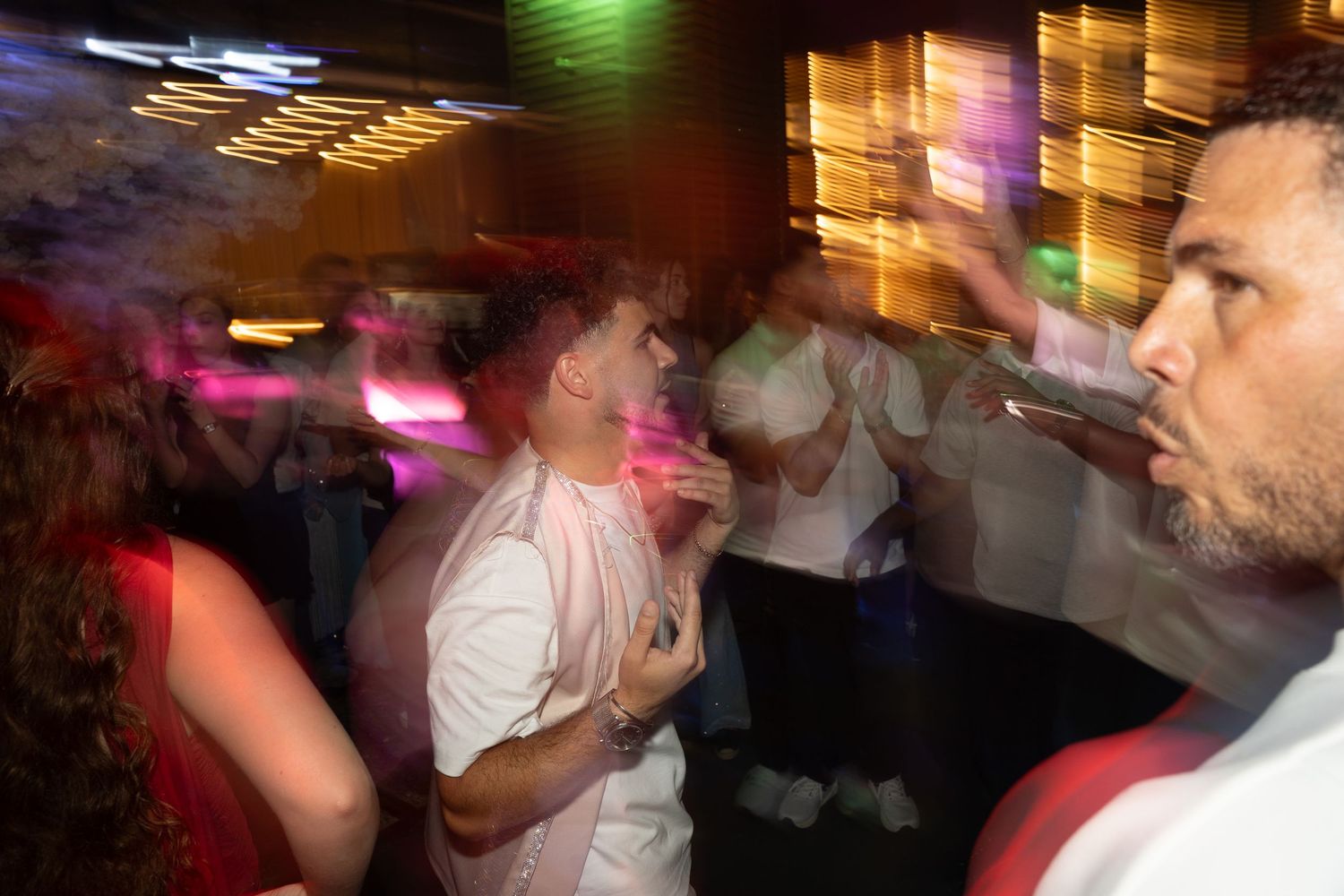 People dancing in a crowded nightclub with colorful lights and smoke filling the dance floor.