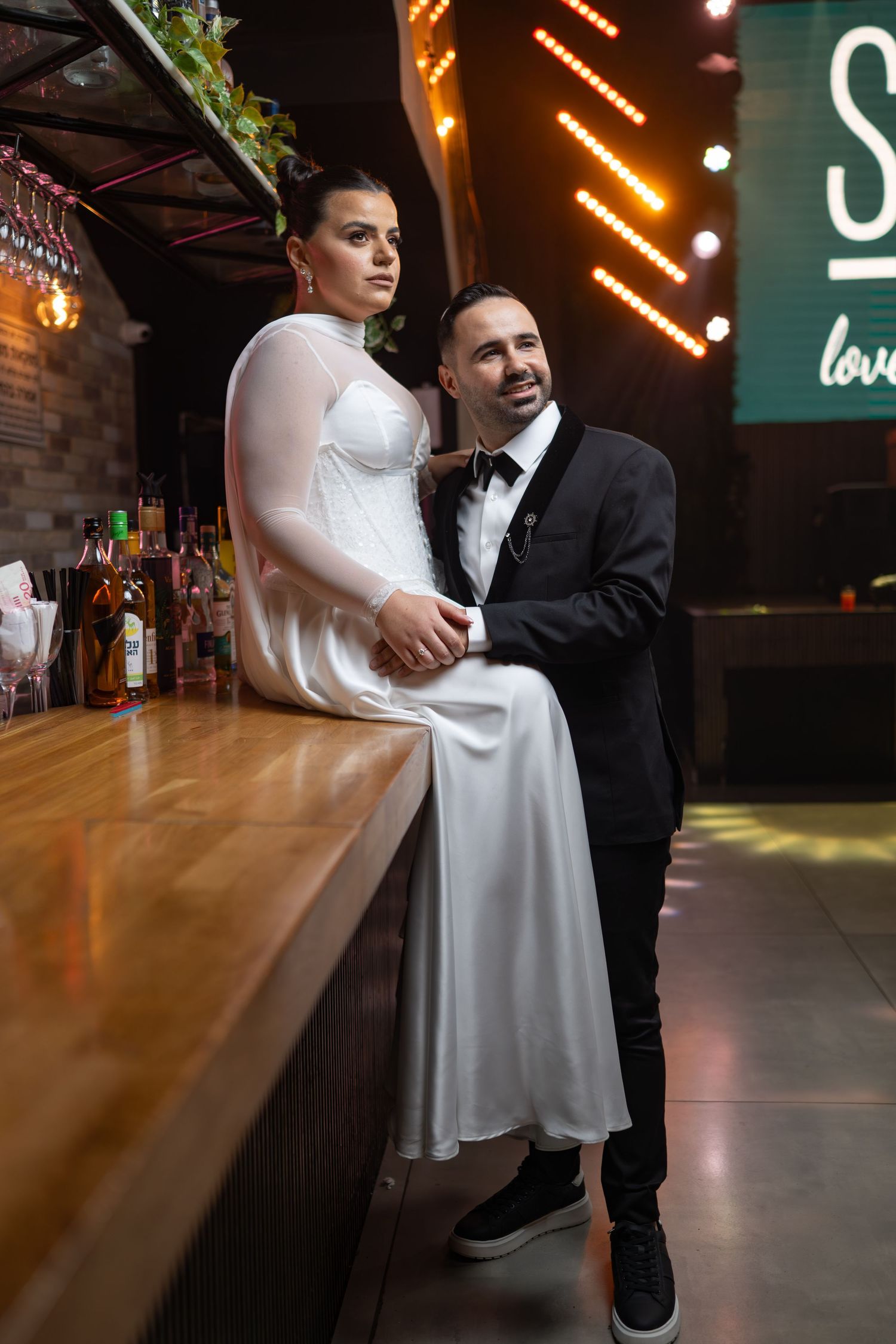 Couple shares intimate moment at illuminated bar with neon signage.