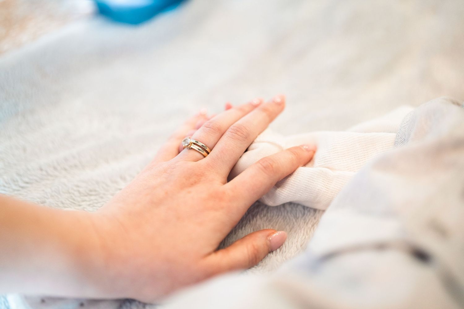 Close-up of an engagement ring on a hand against a soft white background.