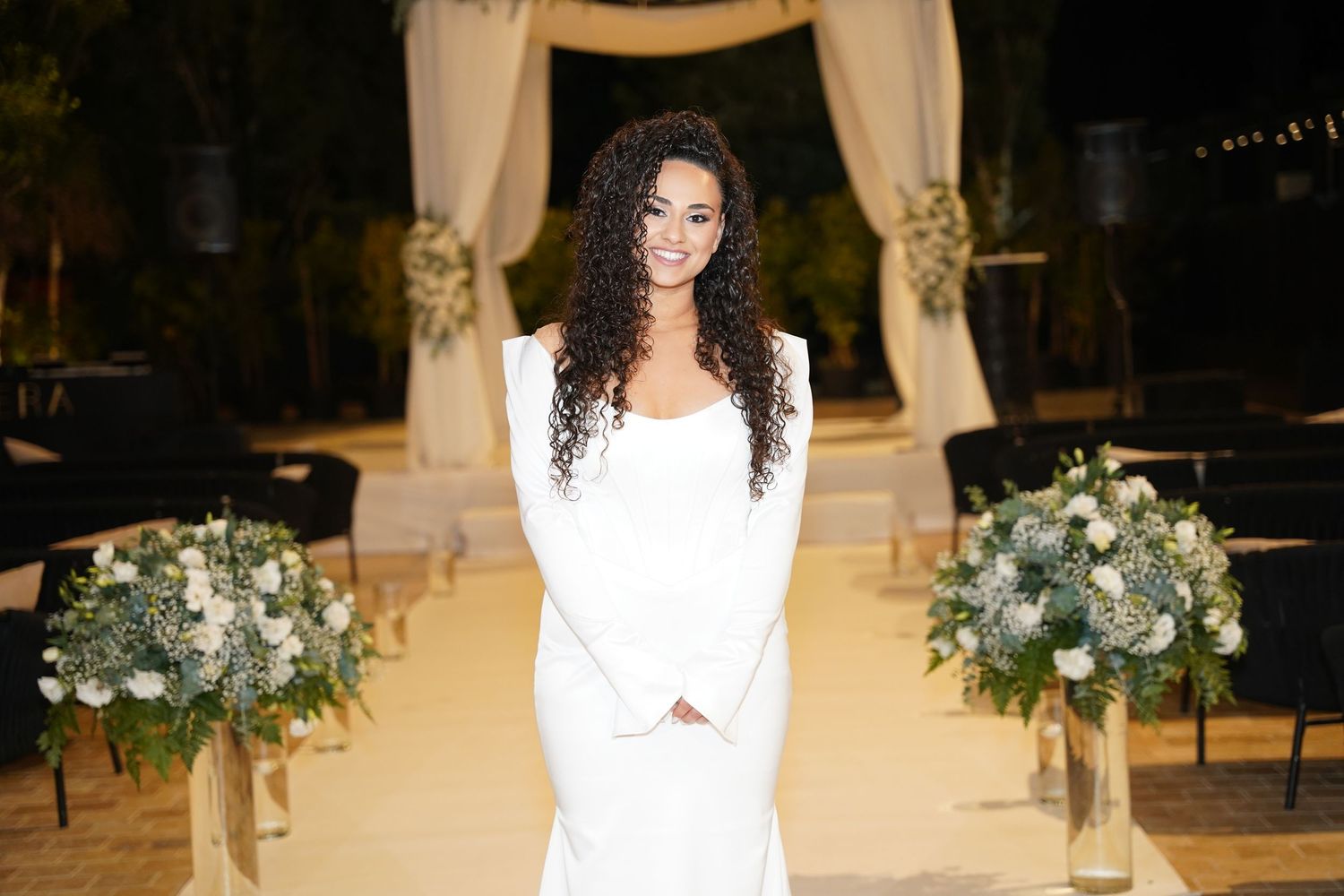 Elegant wedding ceremony setup with white floral arrangements and draping in an indoor venue.