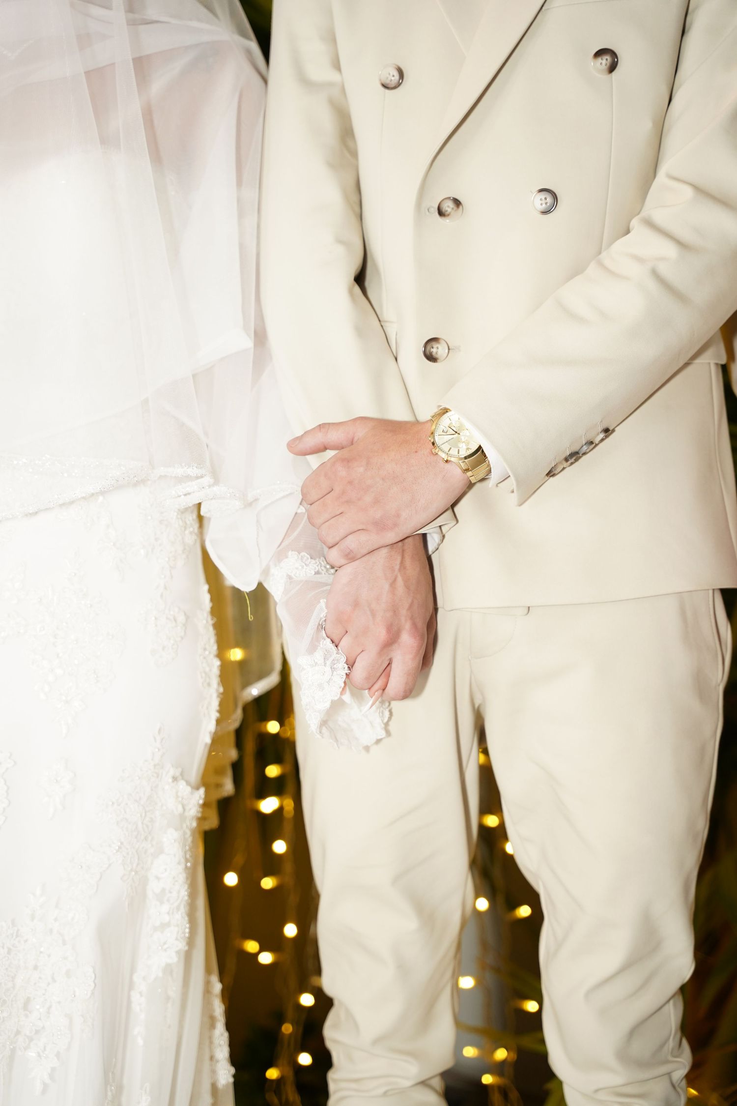 Close-up details of a cream-colored wedding suit and white lace dress during an intimate moment.