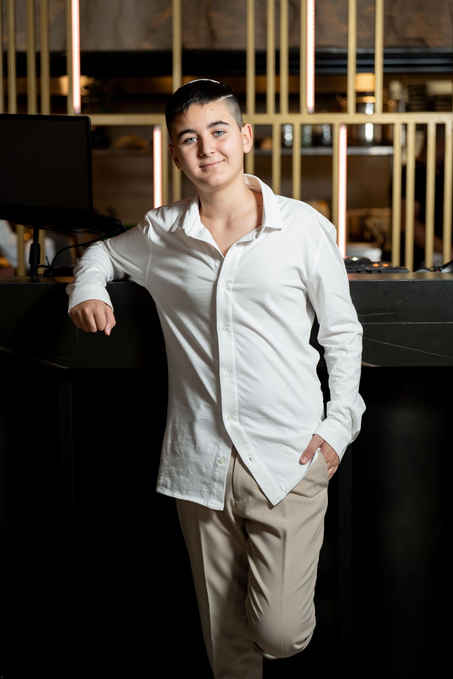 A young child in a white button-down shirt and khaki pants poses against a dark background in a series of photos.