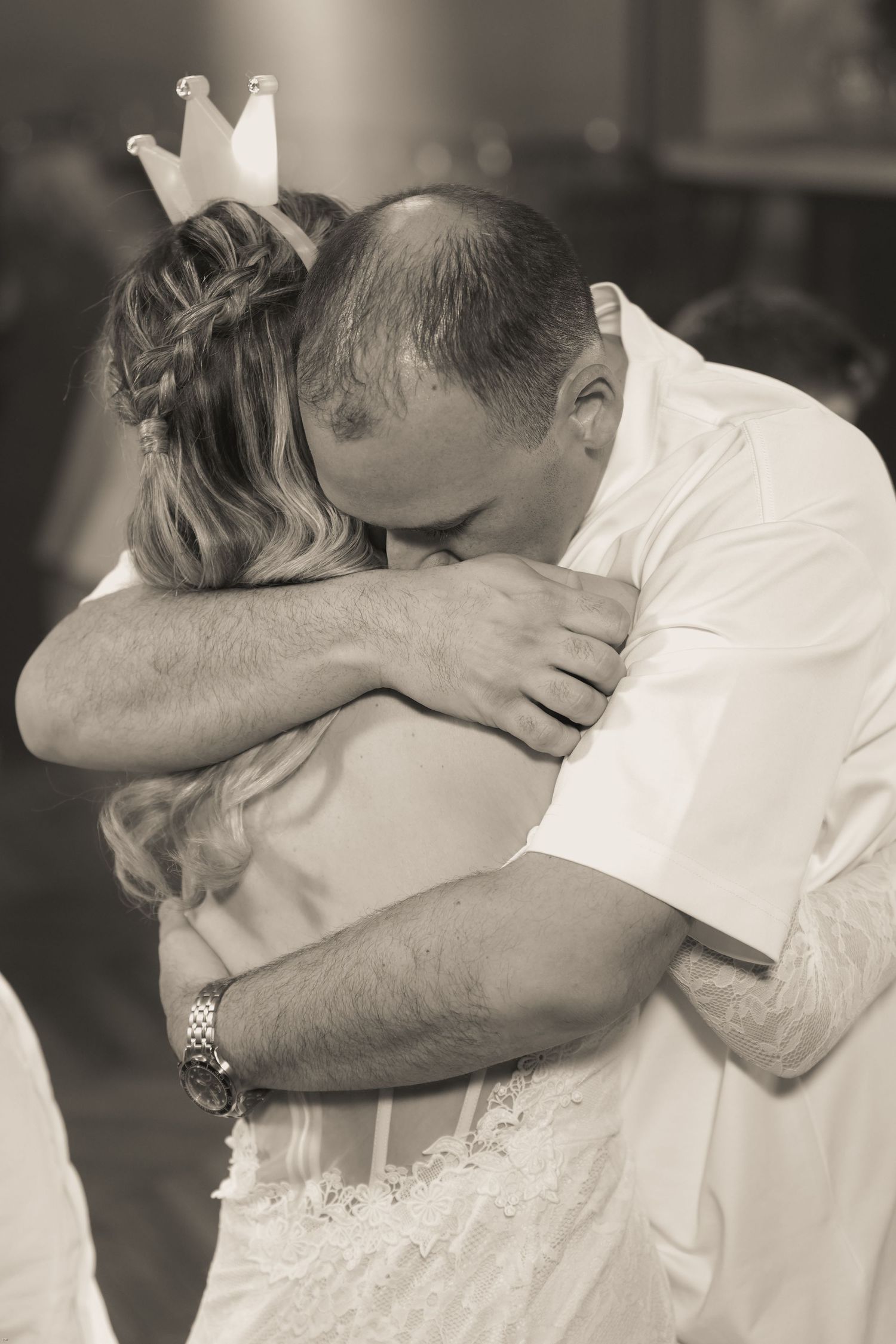 A tender black and white wedding moment showing an emotional embrace between two people, with one wearing a crown.