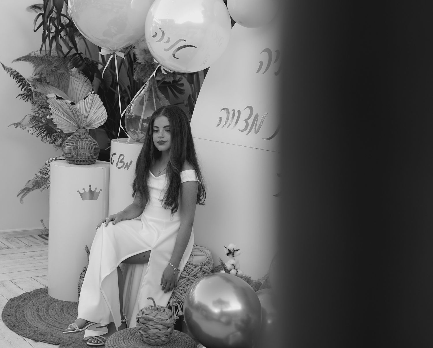 Black and white photo of someone in white sitting against decorative party backdrop.