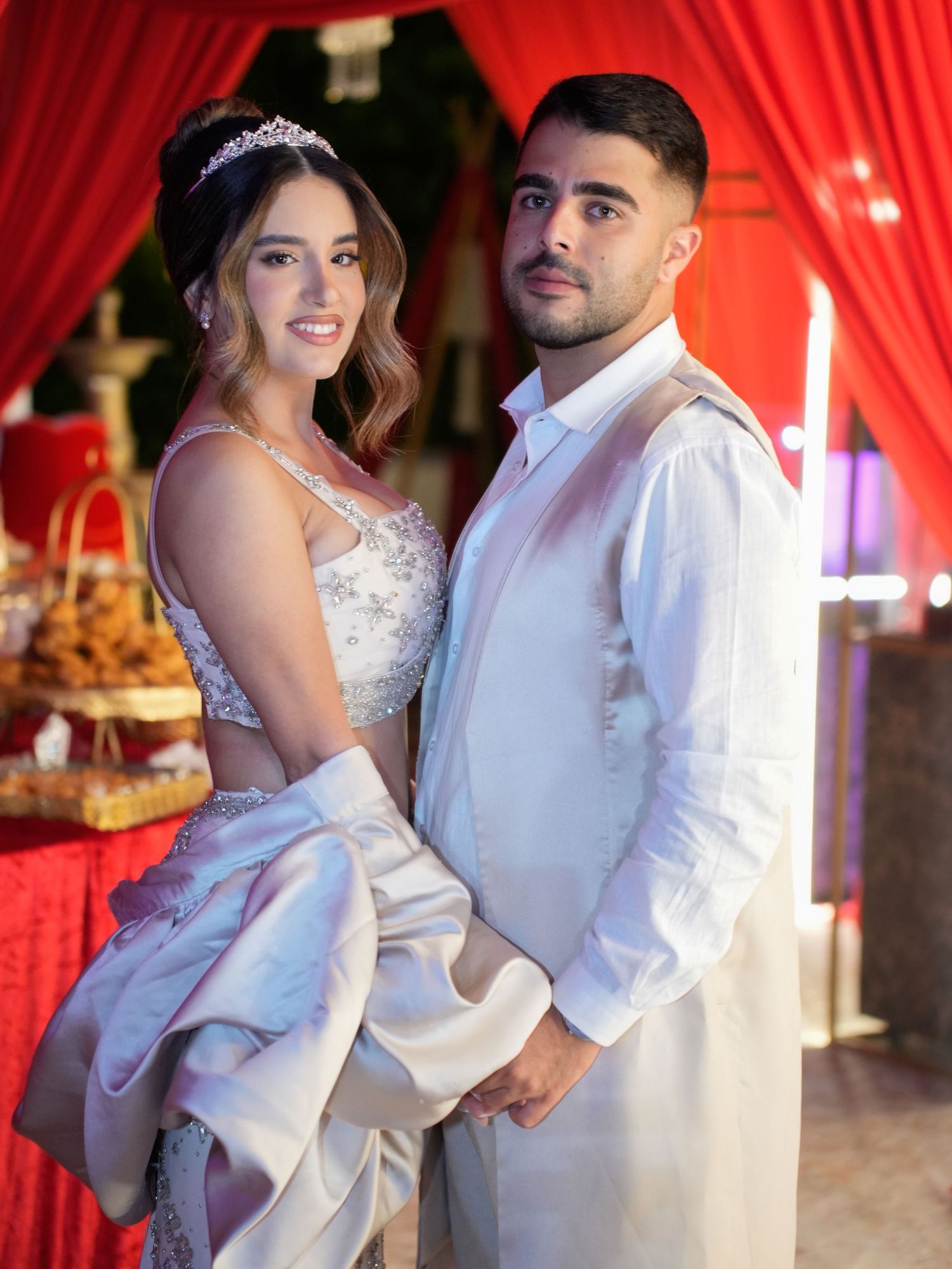 Romantic wedding couple dancing together against red and white draped backdrop.