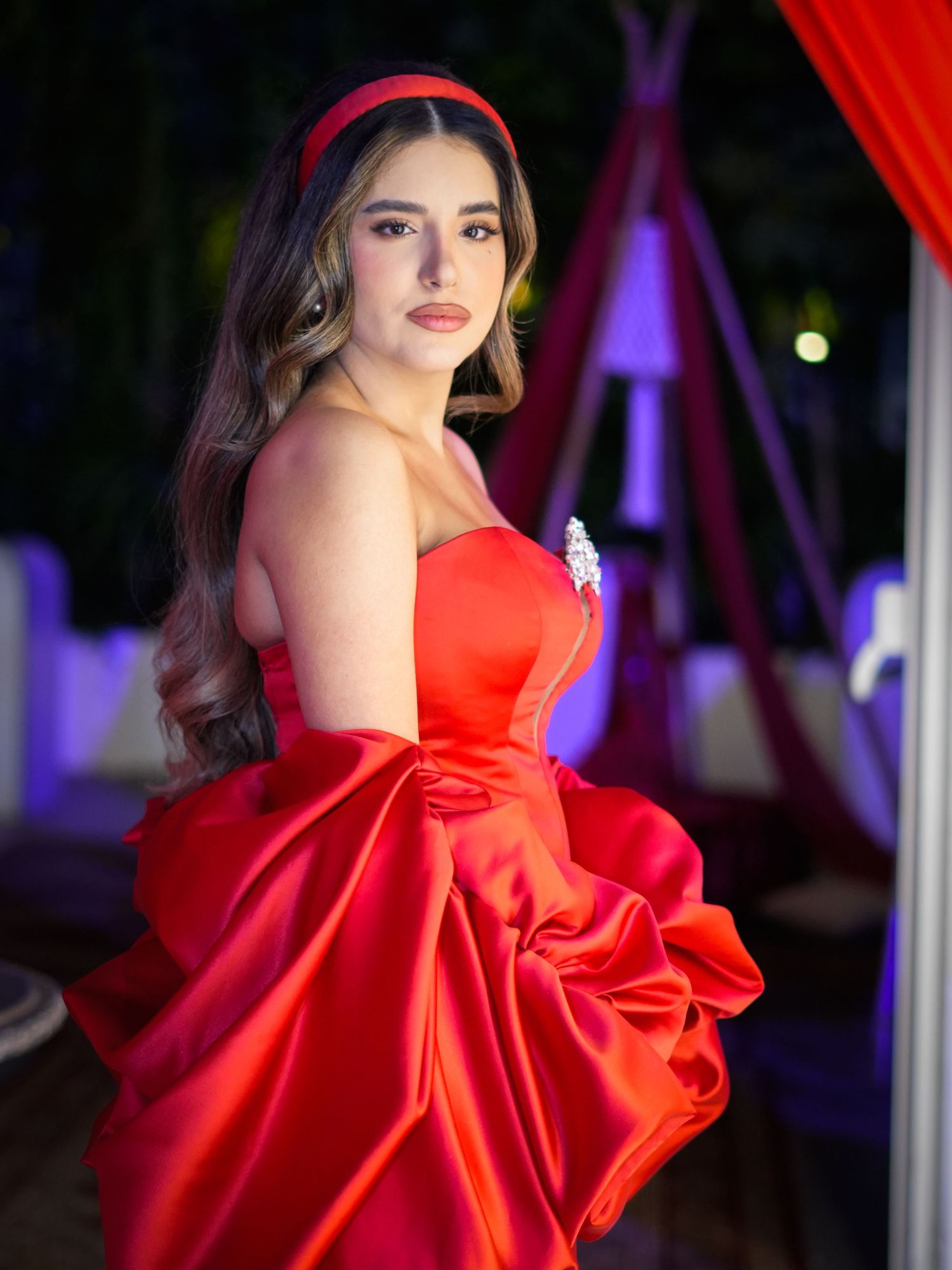 Elegant model in vibrant red satin gown with dramatic ruffled details posing against dark background.