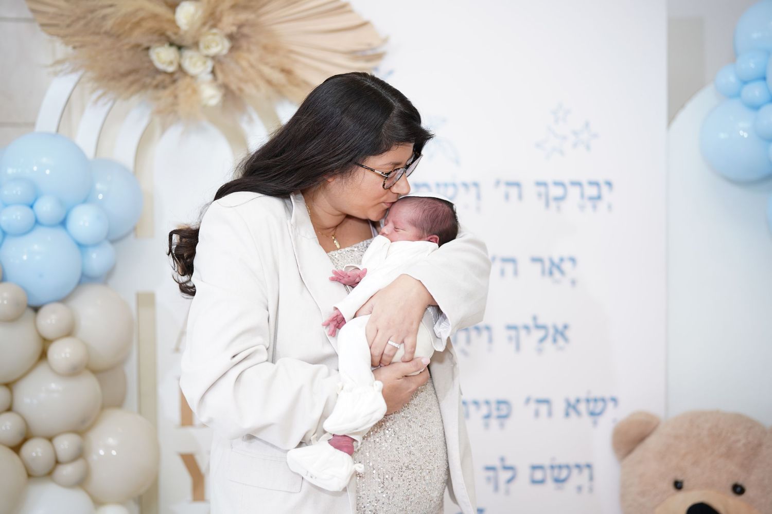 Parent in white holds and kisses newborn baby during celebration.