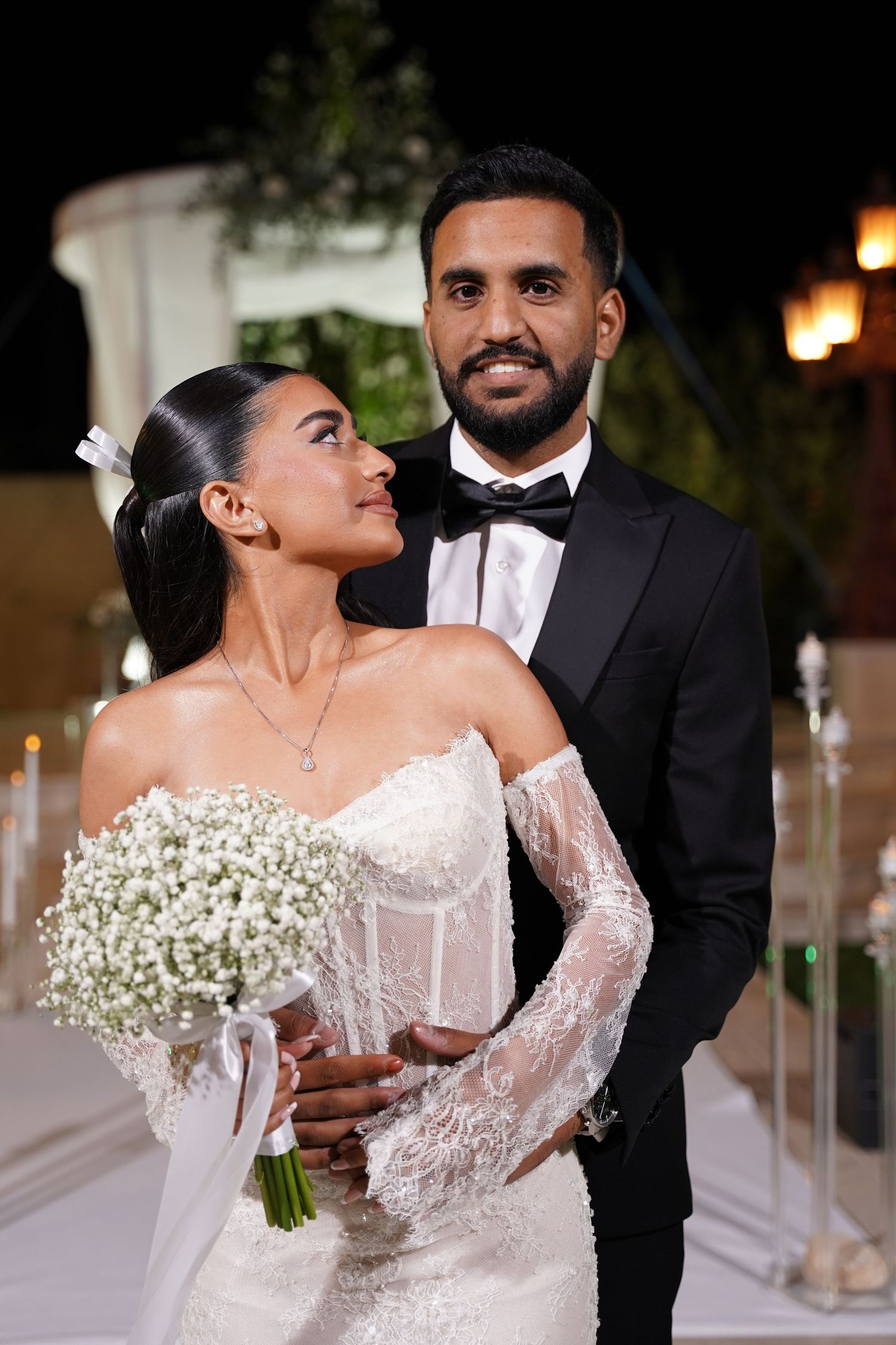 Bride in lace gown holds white bouquet while sharing intimate moments with groom.