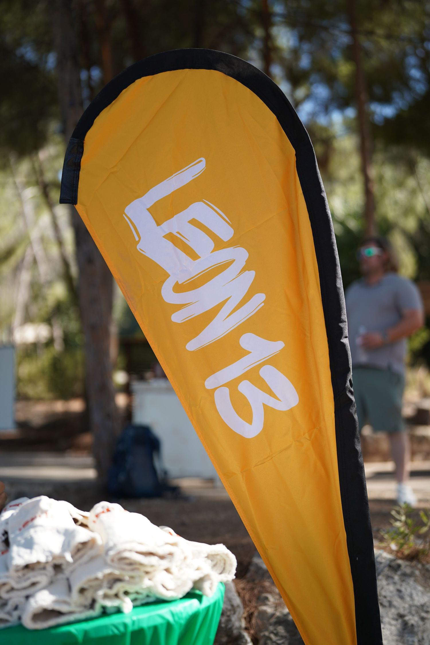 Orange promotional flag with white text displayed outdoors among trees.