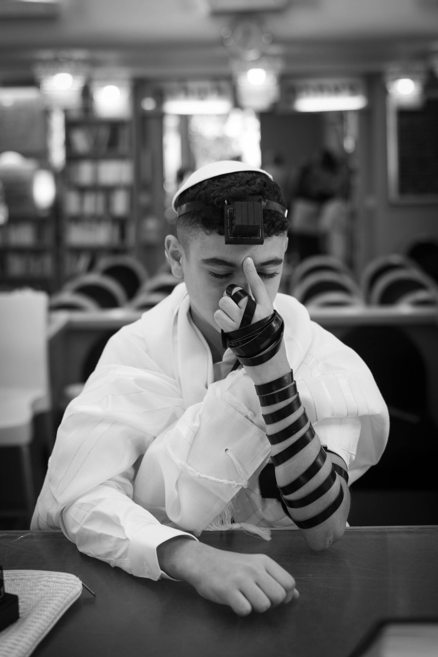 A person in religious attire wraps tefillin while sitting at a table.