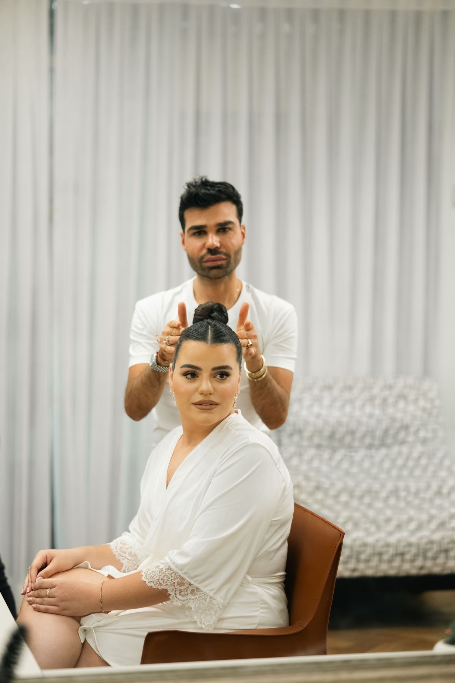A hair styling session in progress with a person seated in a brown chair wearing a white robe.