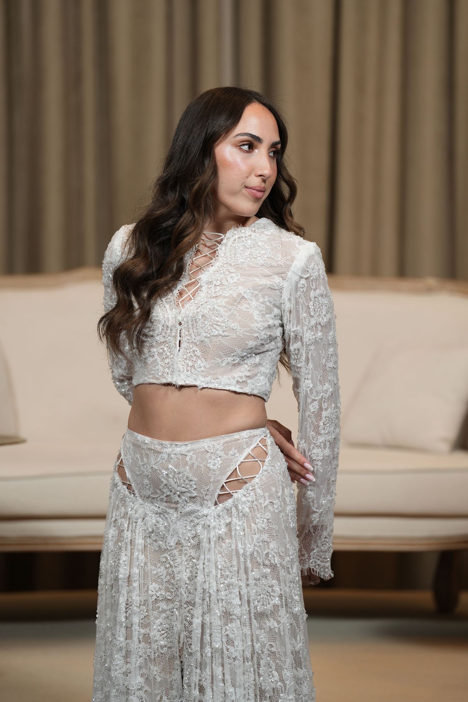 Woman in elegant white lace crop top and skirt set posing gracefully indoors.