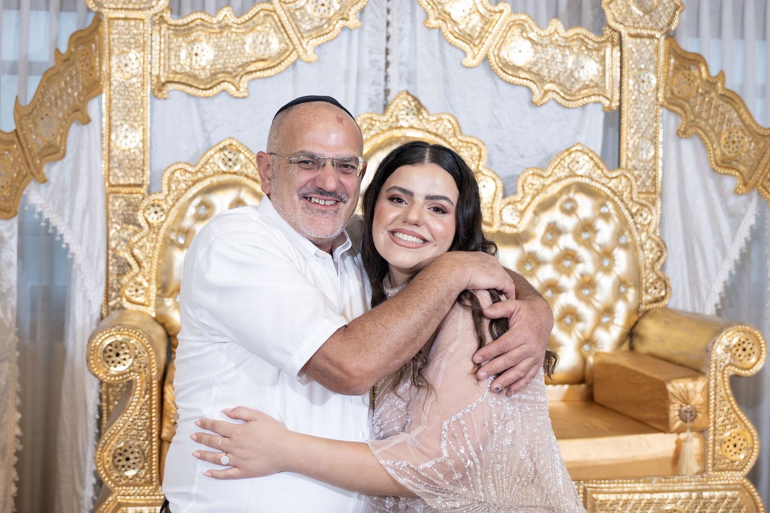 Two people hugging and smiling in front of decorative gold throne setting.